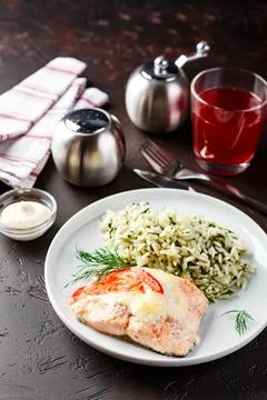 Lunch table with plate of baked red fish with cheese, rice with spinach, set  Stock Photos