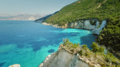Lush green cliffs and vibrant blue bay with a small boat anchored in Kefalonia Stock Footage 309554195