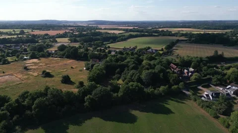 Lush green fields and trees surround a village, with rolling hills in the d.. Stock Footage 340475351