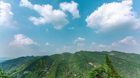 Lush green mountain landscape under a bright blue sky with fluffy clouds Stock Footage 341925500