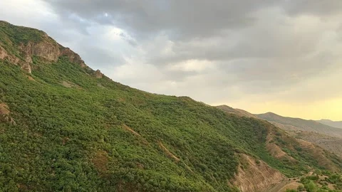 Lush green mountains gradually transition into a valley under a cloudy sky Stock Footage 344345375