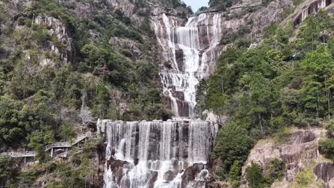 Lush green mountains with multiple cascading waterfalls flowing over rocky Stock Footage 340105986