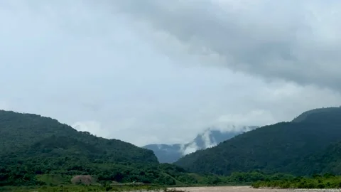 Lush green mountains under a cloudy sky with misty peaks and a winding rive.. Stock Footage 339295872