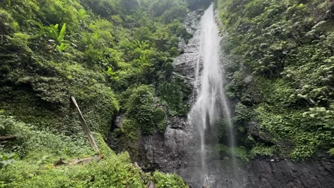 Lush Tropical Waterfall Flowing Down Rocky Cliff, Panning Shot Stock Footage 324851440