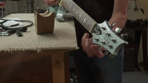 A luthier adjusting strings tension tunes a newly strung guitar by turning pegs Stock Footage 146960577
