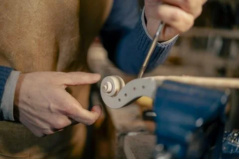Luthier carefully crafting scroll of white violin with chisel in workshop Foto stock
