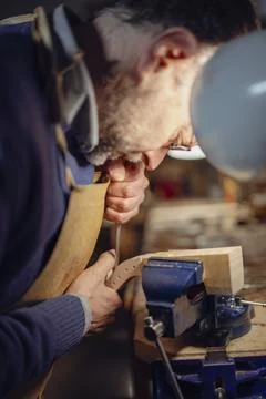 Luthier carefully working on violin scroll in workshop using small chisel and Foto stock