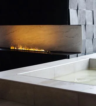 Luxurious bath next to artificial fire in a modern fireplace. Stock Photos