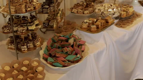 A luxurious dessert table for an event, covered with a white tablecloth and Stock Footage 323636431