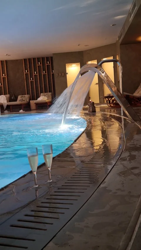 Luxurious indoor spa pool with cascading water and champagne flutes Stock Footage 317874819