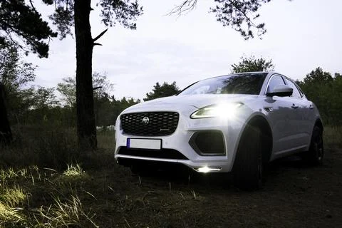 A luxurious white electric Jaguar E-Pace is parked in the evening forest Stock Photos