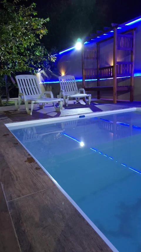 Luxury backyard pool with lounge chairs and blue LED lights at night Stock Footage 312898170