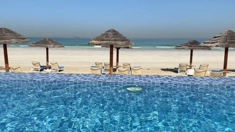Luxury beachfront infinity pool overlooking white sandy beach and calm turquoise Stock Footage 345041528