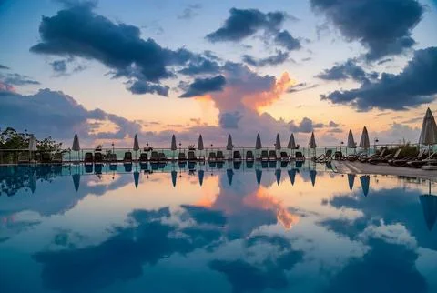 Luxury infinity pool with dramatic cloudy sky reflection at sunset. Stock Photos