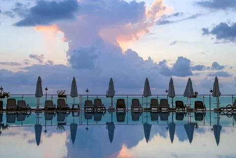 Luxury infinity pool with dramatic cloudy sky reflection at sunset. Stock Photos