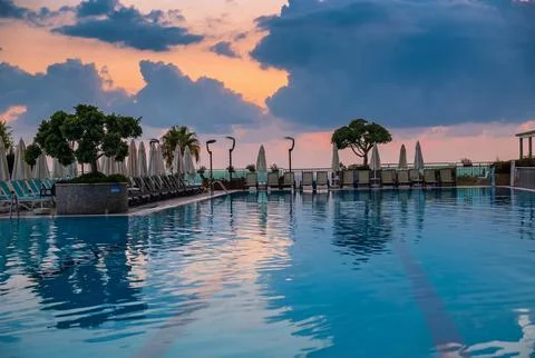 Luxury infinity pool with dramatic cloudy sky reflection at sunset. Stock Photos