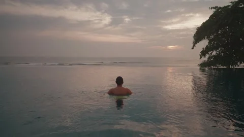 Luxury infinity pool at sunset in Bali with man relaxing ocean view Stockbeeldmateriaal 331061473