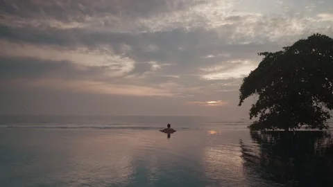 Luxury infinity pool at sunset in Bali with man relaxing ocean view Stock Footage 331062341