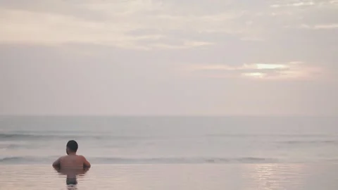 Luxury infinity pool at sunset in Bali with man relaxing ocean view Stock Footage 331065750