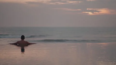 Luxury infinity pool at sunset in Bali with man relaxing ocean view Stock Footage 331066603