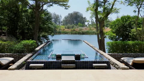 Luxury resort infinity pool overlooking tranquil lake surrounded by lush Stock Footage 271724986