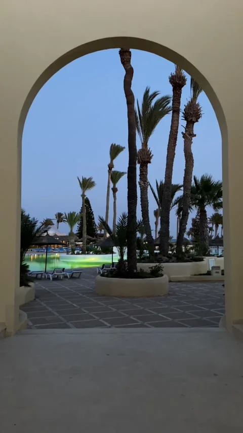 Luxury resort pool at dusk through archway palm trees Djerba Tunisia HD vertical 스톡 동영상 342078474