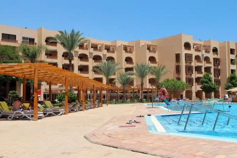 Luxury resort swimming pool area with sunbeds and hotel building background Stock Photos