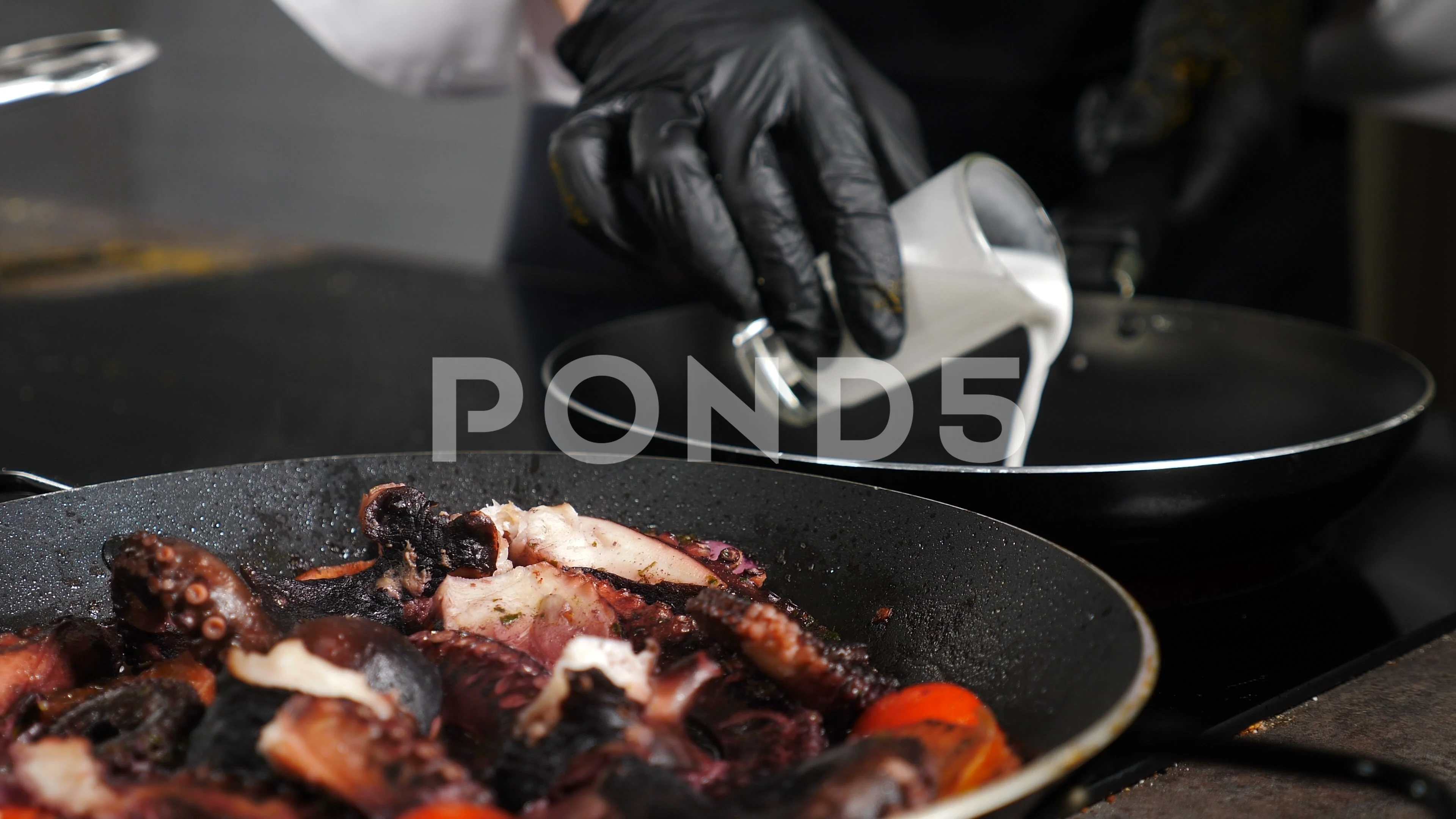 The chef cooks small octopus on a metal frying pan at the