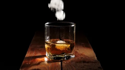 Luxury whiskey. Ice cubes fall with splashes into a glass with golden whisky Stock Footage