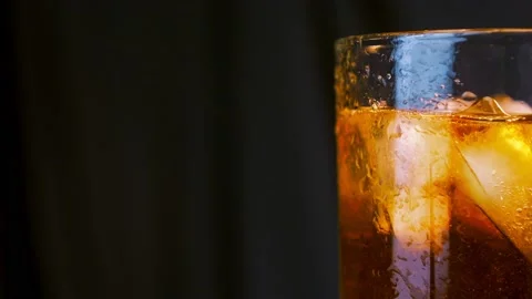 Luxury whiskey. Ice cubes fall with splashes into a glass with golden whisky on Stock-Footage 202632584