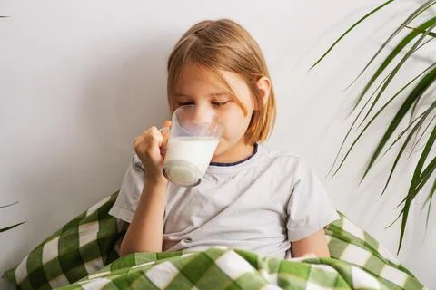 Lying in bed, a 9-10-year-old boy with flowing locks enjoys a glass of milk.. Stock Photos