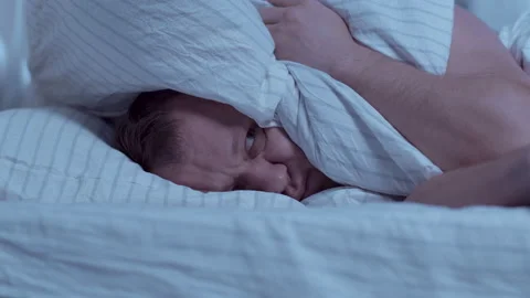 Lying in bed at night, a man cannot sleep, covers his head with a pillow Stock Footage 153862615