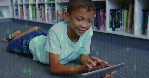 Lying boy wearing teal tee, dark jeans holding tablet, browsing in library with Foto stock