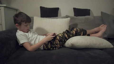 Lying on the couch, a student plays a game on his smartphone. Children's depende Stock Footage 146316617