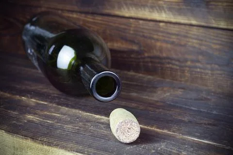 Lying empty wine bottle with cork nearby on plank wooden surface Stock Photos