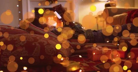 Lying girl using smartphone on patterned rug in festive room, with string lights Stock Photos