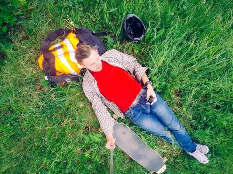 Lying in the grass, the Guy is resting after riding a longboard. Stock Photos