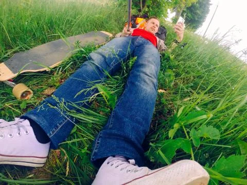 Lying in the grass, the Guy is resting after riding a longboard. Stock Photos