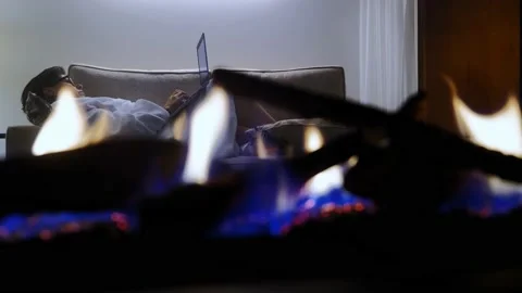 Lying On a Sofa in a Room Behind a Fireplace and Using Laptop and Smartphone Stock Footage 203776907