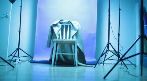 Mac coat hangs on a back of a wooden chair in an empty blue lit photo studio Stock Photos
