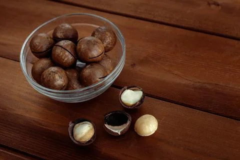 Macadamia with kernel nuts and nutshell in bowl on wooden table Stock Photos
