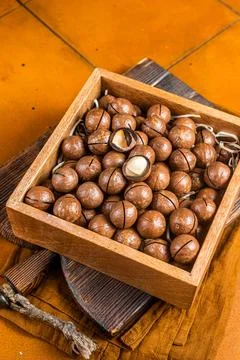 Macadamia natural nuts in a box. Orange background. Top view Stock Photos