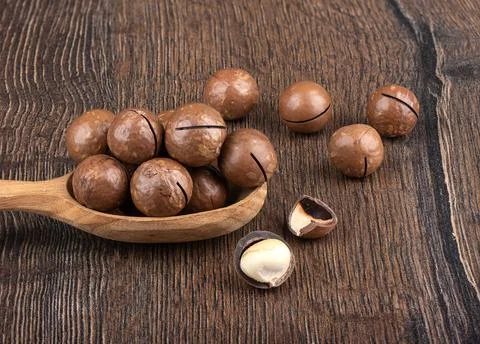 Macadamia nuts and nut shells on a wooden background. Stock Photos