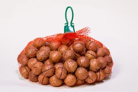 Macadamia nuts in a red mesh bag on a white background Stock Photos
