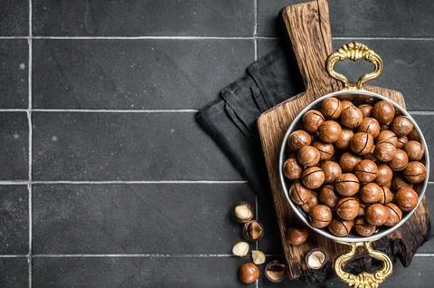 Macadamia nuts in a shell ready to eat. Black background. Top view. Copy spac Stock Photos