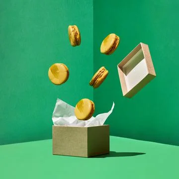 Macaron floating from craft box with levitating box's cover on green back Stock Photos
