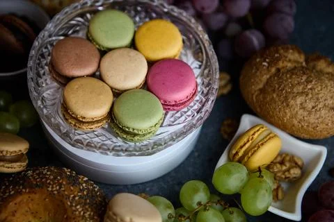 Macaron stack in small bowl with grapes and bread rolls rustic tabletop Stock-Fotos