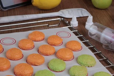 Macarons halves on baking mat on kitchen table. Orange and green cookie cutters Stock Photos