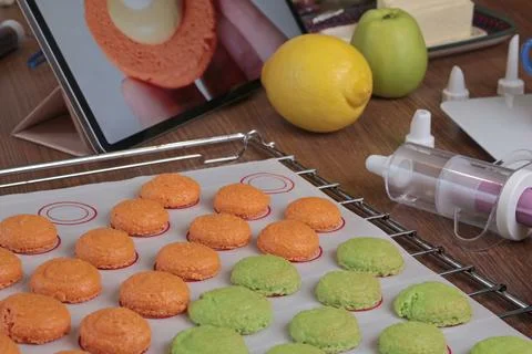 Macarons halves on baking mat on kitchen table. Orange and green cookie cutters Stock Photos