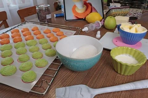 Macarons halves on baking mat on kitchen table. Orange and green cookie cutters Stock Photos